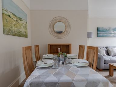 A dining area with a table set for four with plates glasses and cutlery next to a living room with a sofa and paintings on walls at Nuke in Weymouth
