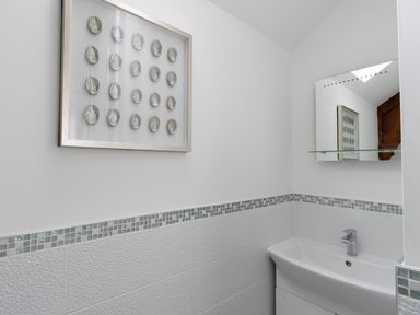 A small bathroom corner with a white sink below a mirror and a wall decoration above the tiling at Nuke in Weymouth
