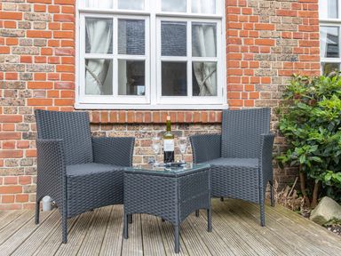 Two dark wicker chairs and a wicker table with a bottle of wine and two glasses on a wooden deck outside a brick building at Nuke in Weymouth