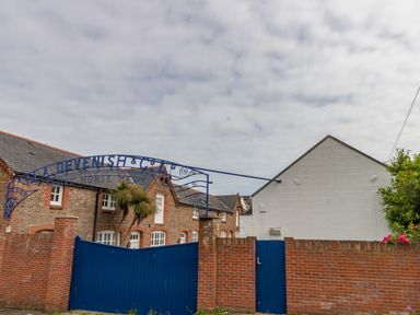 A brick building with arched windows behind a blue gate and brick wall under a cloudy sky at Nuke in Weymouth