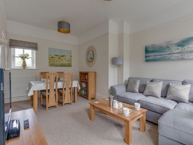 A living room with a gray sofa wooden coffee table dining table with chairs bookshelf and paintings at Nuke in Weymouth