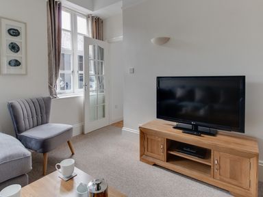 A living room with a television on a wooden stand and a grey chair by a window at Nuke in Weymouth