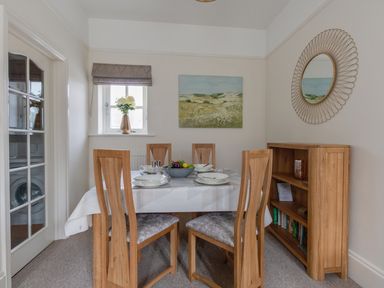 A dining room with a wooden table set for four surrounded by wooden chairs and a small wooden shelf unit at Nuke in Weymouth
