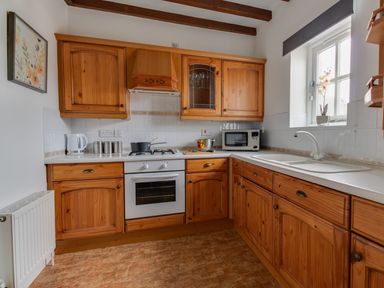 A kitchen with wooden cabinets a white oven a microwave a white kettle and a window with a flower pot at Nuke in Weymouth