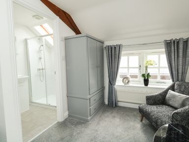 A room with a gray wardrobe gray curtains a patterned chair and an en suite bathroom with a shower at Nuke in Weymouth