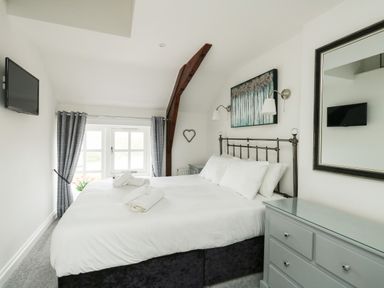 A bedroom with a bed with white linens and rolled towels a tv mounted on the wall a dresser with a mirror and curtains on the window at Nuke in Weymouth