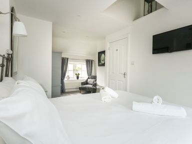A bedroom with a white bed and rolled towels a grey armchair near a window with grey curtains and a wall-mounted television in Nuke Weymouth