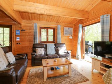 A wooden living room with two brown leather sofas a wooden coffee table a flat screen tv and a door opening to an outdoor area with a barbecue at Heron Lodge in Badwell Ash