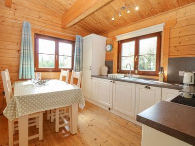 A kitchen with a dining table covered with polka dot tablecloth and white chairs near windows and cabinets at Heron Lodge in Badwell Ash