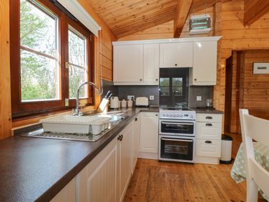 A kitchen with white cabinets a stove a sink and large windows at Heron Lodge in Badwell Ash