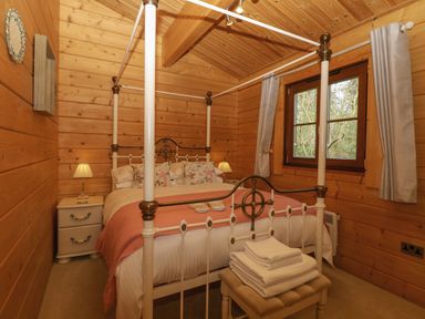 A bedroom with a four-poster bed bedside tables lamps and a window with curtains at Heron Lodge in Badwell Ash