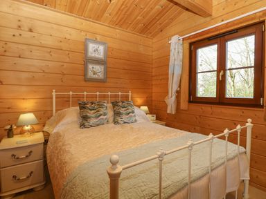 A bedroom with a bed a window two bedside tables and lamps at Heron Lodge in Badwell Ash
