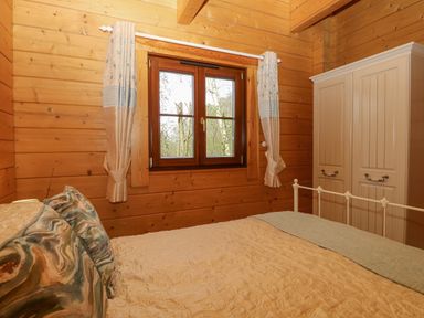 A bedroom with a bed pillows window with curtains and a wardrobe at Heron Lodge in Badwell Ash