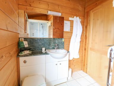 A bathroom with a white sink and cabinet wooden walls and two white robes hanging on hooks at Heron Lodge in Badwell Ash