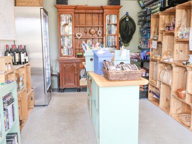 A small shop with wooden shelves stocked with various items and a wooden cabinet with books at Heron Lodge in Badwell Ash