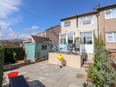 A backyard patio with a glass-enclosed deck table with chairs shed and plants at Heddfan in Conwy