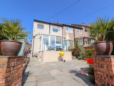 A paved backyard with potted plants and a glass-enclosed patio attached to a row house at Heddfan in Conwy
