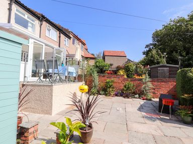 A paved backyard with patio furniture umbrella plants and a small shed at Heddfan in Conwy