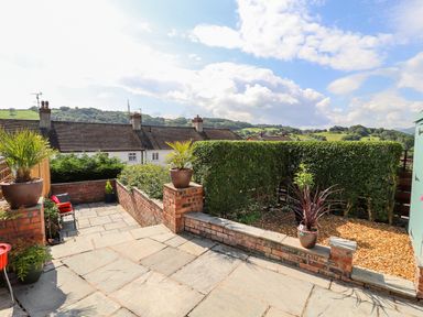An outdoor patio area with stone tiles brick walls potted plants and bushes with hills in the background at Heddfan in Conwy