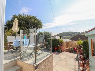 An outdoor patio area with a table and chairs behind glass railing and a garden walkway at Heddfan in Conwy