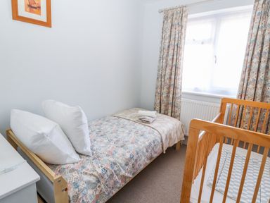 A small bedroom with a single bed, a wooden crib, a white nightstand, and a window with floral curtains at Heddfan in Conwy