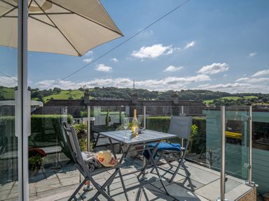A balcony with a table and two chairs with a bottle and glasses under an umbrella at Heddfan in Conwy