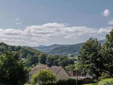 A rural landscape with houses trees and hills under a partly cloudy sky at Heddfan in Conwy