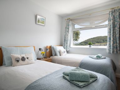 A bedroom with two single beds with folded towels on them beside a window and a nightstand with lamps at Heddfan in Conwy