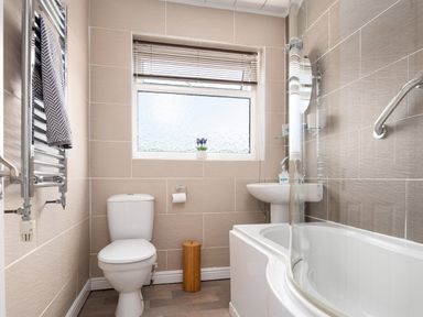 A bathroom with a toilet, towel rack, window, sink, and bathtub at Heddfan in Conwy
