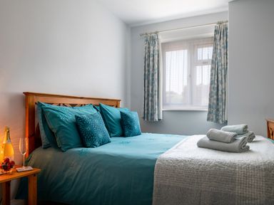 A bedroom with a wooden bed with teal bedding and patterned curtains at Heddfan in Conwy