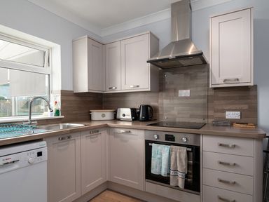 A kitchen with a sink dishwasher toaster kettle stove and cabinets at Heddfan in Conwy