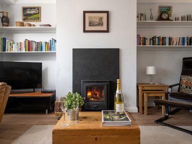 A living room with a wood burning stove bookshelves a television and a wooden coffee table at Heddfan in Conwy