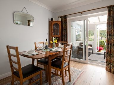 A dining area with a wooden table and chairs set with plates and glasses next to a glass door leading to a porch at Heddfan in Conwy