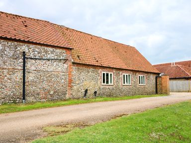 An exterior view of a building with stone walls red tiled roof four white framed windows and a gravel path with grass on the side at Far Barn in Fakenham