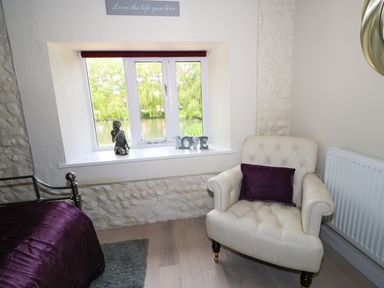 A room with a window seat displaying a figurine and love letters a white armchair with a purple cushion and part of a bed with a purple bedspread at Far Barn in Fakenham