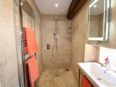 A bathroom with beige tiled walls a walk-in shower a white sink with a mirror and orange towels at Far Barn in Fakenham