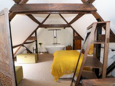 A bedroom with a yellow blanket on the bed a bathtub and wooden beams at Far Barn in Fakenham