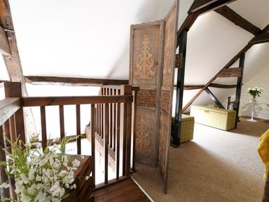 A loft area with wooden railing and carved wooden screen with green storage ottomans and flowers on a small table at Far Barn in Fakenham