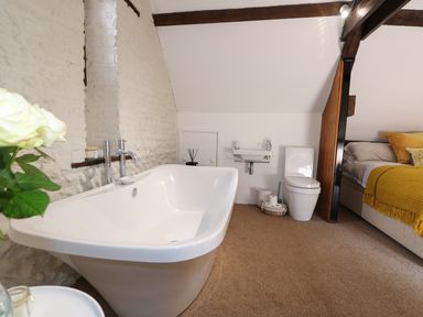 A bathroom with a bathtub toilet and sink next to a bedroom with a bed and yellow blanket at Far Barn in Fakenham