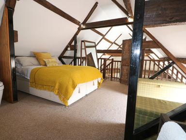 A loft bedroom with a bed covered in a yellow blanket and a standing mirror at Far Barn in Fakenham