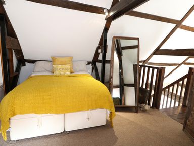 A bedroom with a bed covered in a yellow blanket and pillows next to a full length mirror and wooden beams at Far Barn in Fakenham