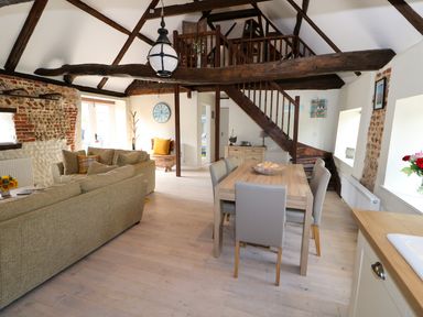 A living and dining area with sofas, dining table, wooden beams, staircase leading to a loft at Far Barn in Fakenham