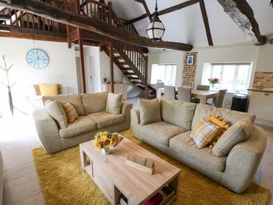 A living room with beige sofas and a wooden coffee table on a yellow rug at Far Barn in Fakenham