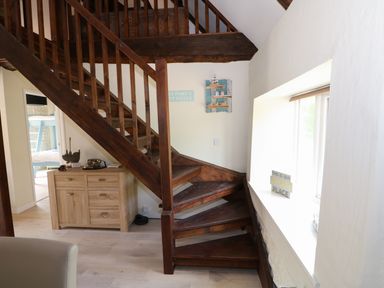 A wooden staircase next to a window and a cabinet with decorative items at Far Barn in Fakenham