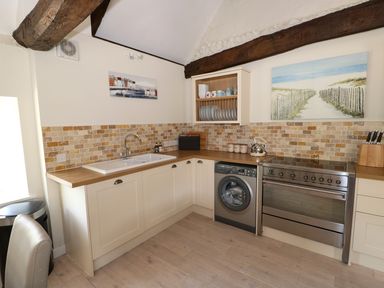 A kitchen with a sink stove washing machine and wall-mounted dish rack at Far Barn in Fakenham