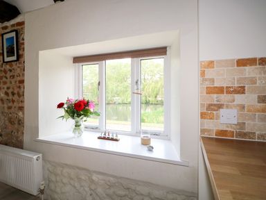 A window with flowers in a vase and small decorative items on the sill at Far Barn in Fakenham