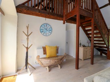 An entryway with a wooden coat rack holding an umbrella a wooden bench with a yellow cushion a blue wall clock a wooden staircase and a small cabinet with decorations at Far Barn in Fakenham
