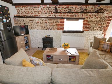 A living room with beige sofas yellow cushions a wooden coffee table and a stone wall at Far Barn Fakenham