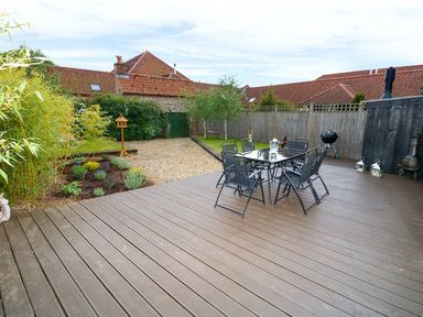 An outdoor patio with a table and six chairs next to a wooden fence and garden at Far Barn in Fakenham