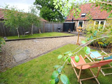 A garden with deck chairs a bird feeder a gravel path and trees at Far Barn in Fakenham
